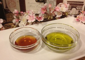 Long shot of two bowls, one with honey and one with olive oil, on a white surface surrounded by flowers