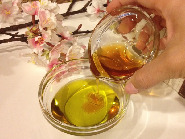 Close-up of a hand pouring honey from a bowl into another bowl with olive oil