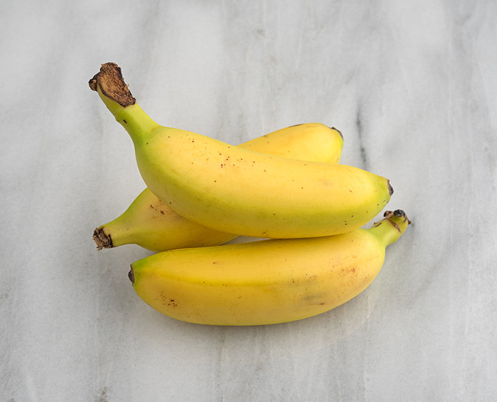 A stack of 3 mini bananas on a marble style background