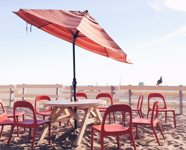 Photo of Back on the Beach Cafe with a round table and red chairs under a red umbrella on the beach