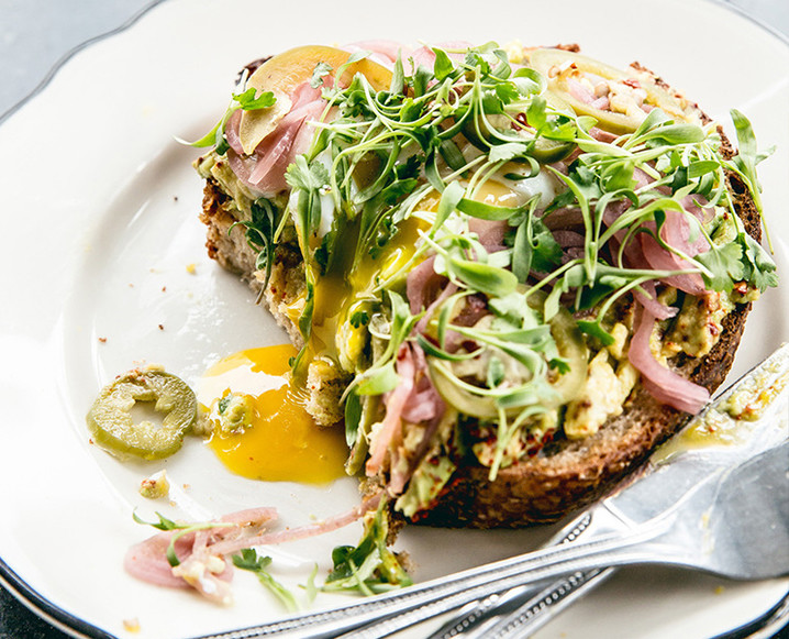 Close up of a white plate with half-eaten egg, ham and salad topped toast