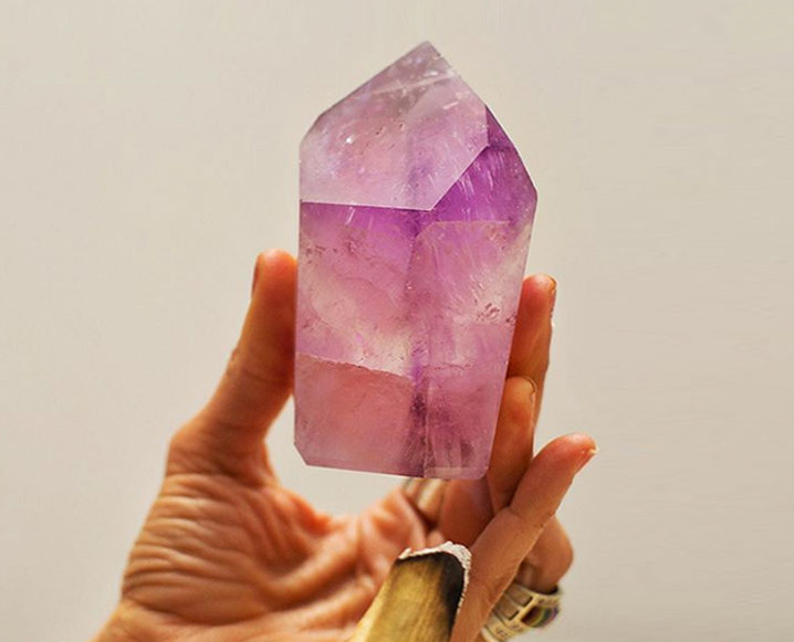 Close-up of a hand holding a pink crystal for cleansing negative energy