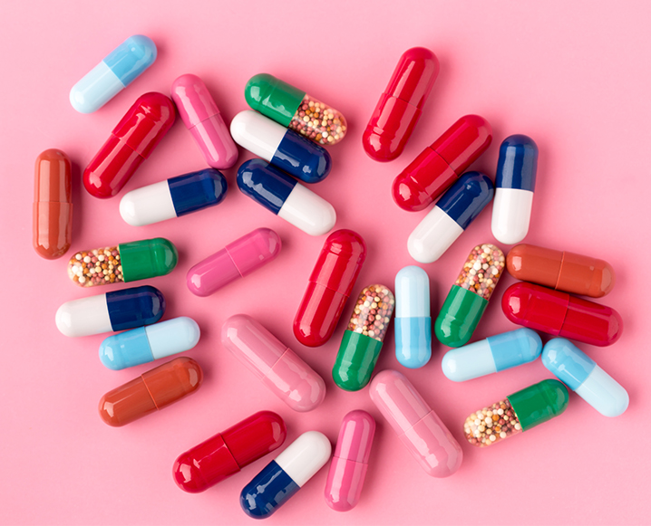 Different sizes and colors of pills for quitting adderall on a bright pink background