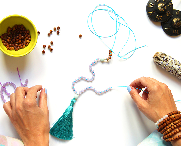 Hands making a mala with beads, string, tassel and other items